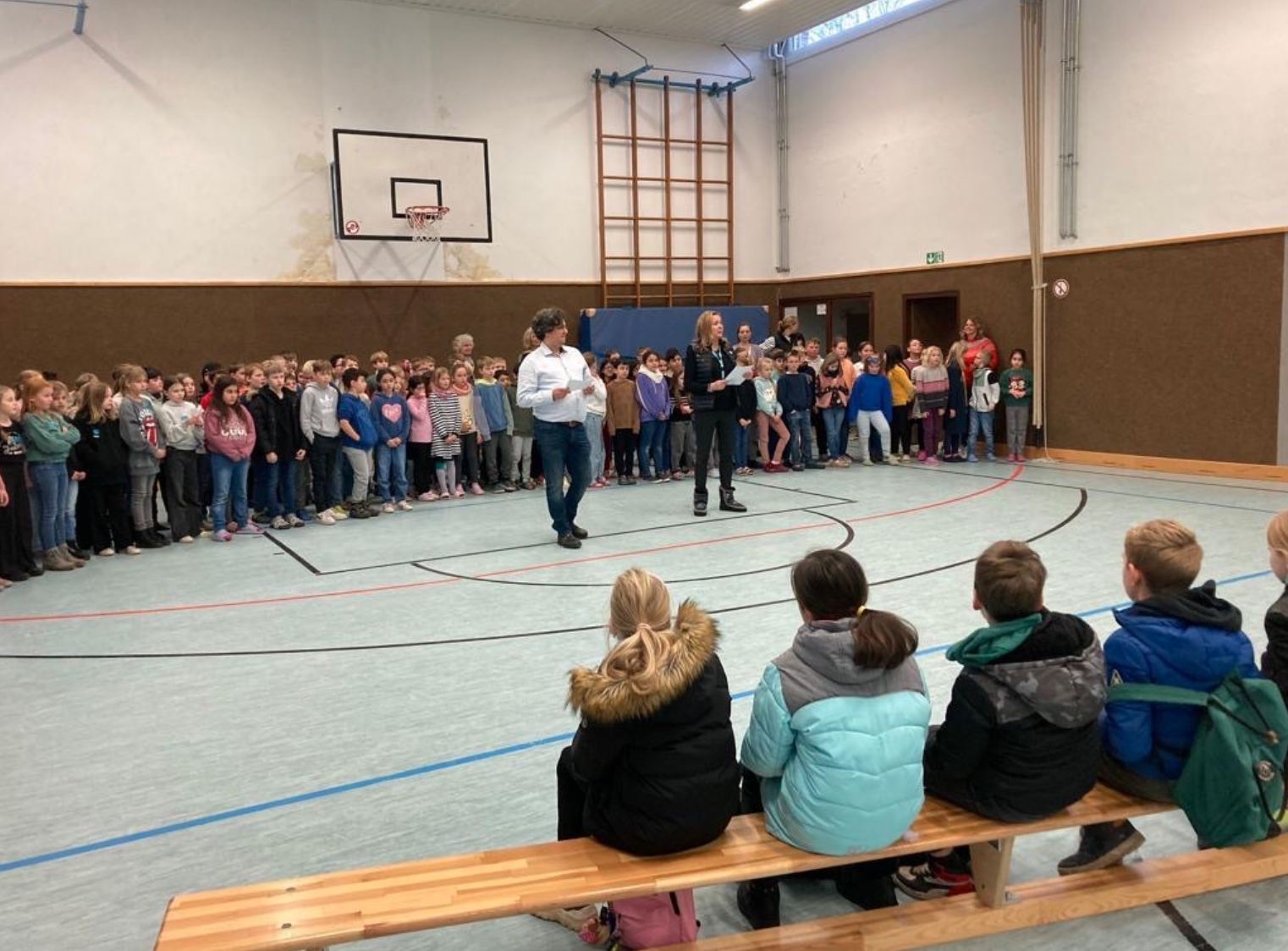 Herr Brömling ebenso wie Frau Sienema begrüßen die Kinder der Emmaschool. Die Kinder der Clemens-Dülmer-Schule versammelten sich hierzu alle in der Sporthalle